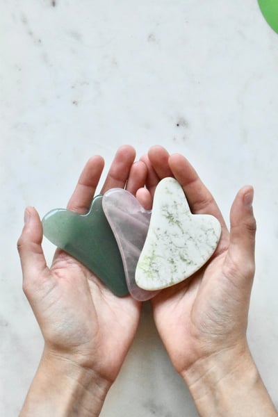 Hands holding heart-shaped gua sha stones